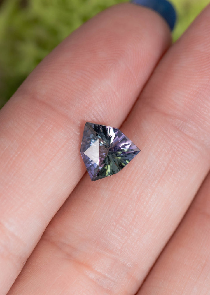 1.66 carat mermaid teal green purple Tanzanite trillion resting on finger, precision custom geometric cut gemstone from Tanzania highlighting symmetry, vivid multicolor sparkle and high clarity for bespoke fine jewelry