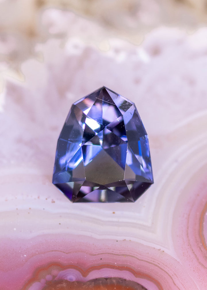 1.66 carat teal green blue purple Tanzanite custom shield modified brilliant displayed on stone surface, Tanzania origin gemstone highlighting symmetry, deep color saturation and precision faceting for bespoke jewelry