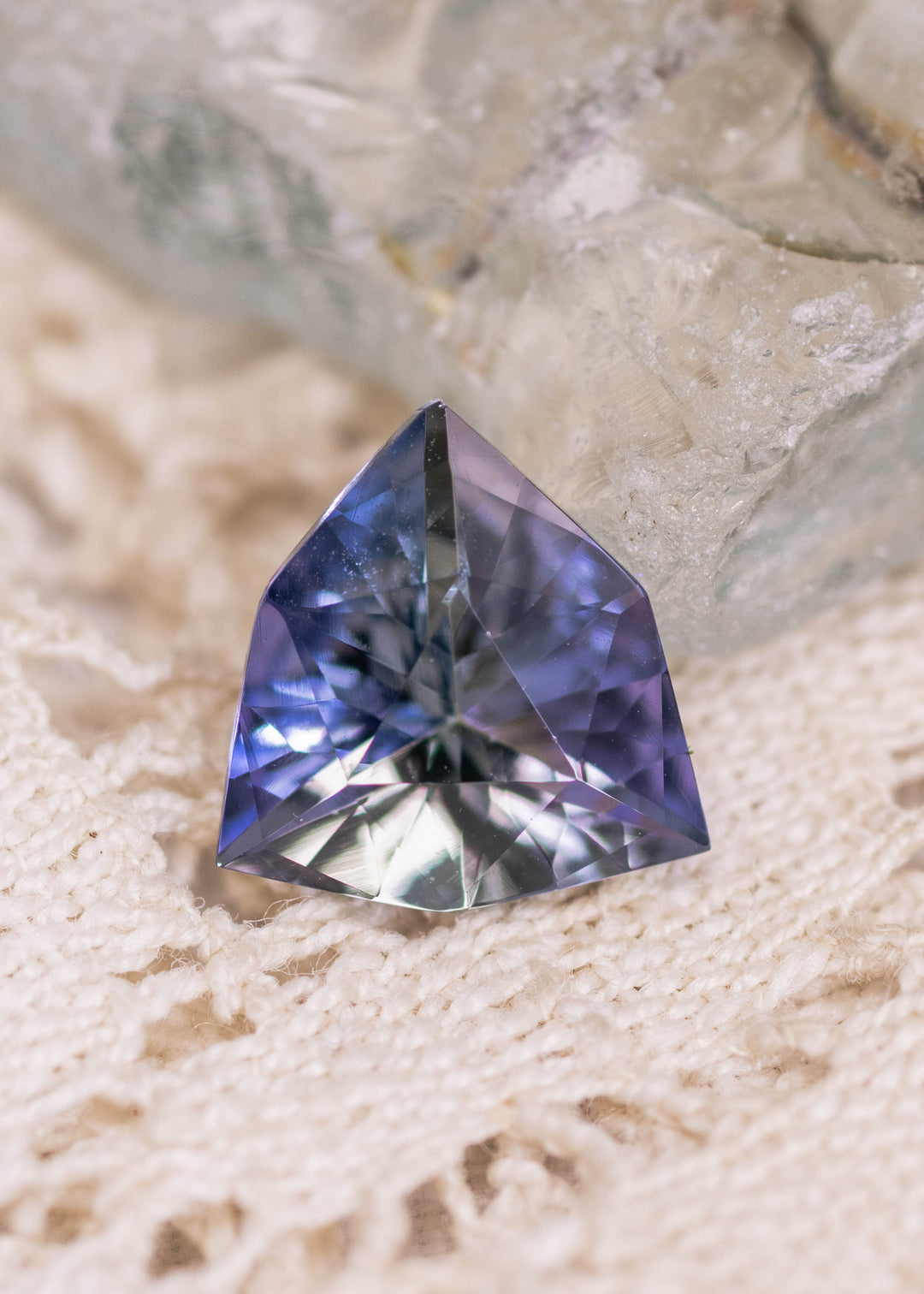 1.66 carat mermaid teal green purple Tanzanite custom geometric trillion displayed on lace and crystal surface, precision faceted gemstone from Merelani Hills Tanzania showing vivid color shift, sharp triangular symmetry and brilliant center reflections for custom jewelry