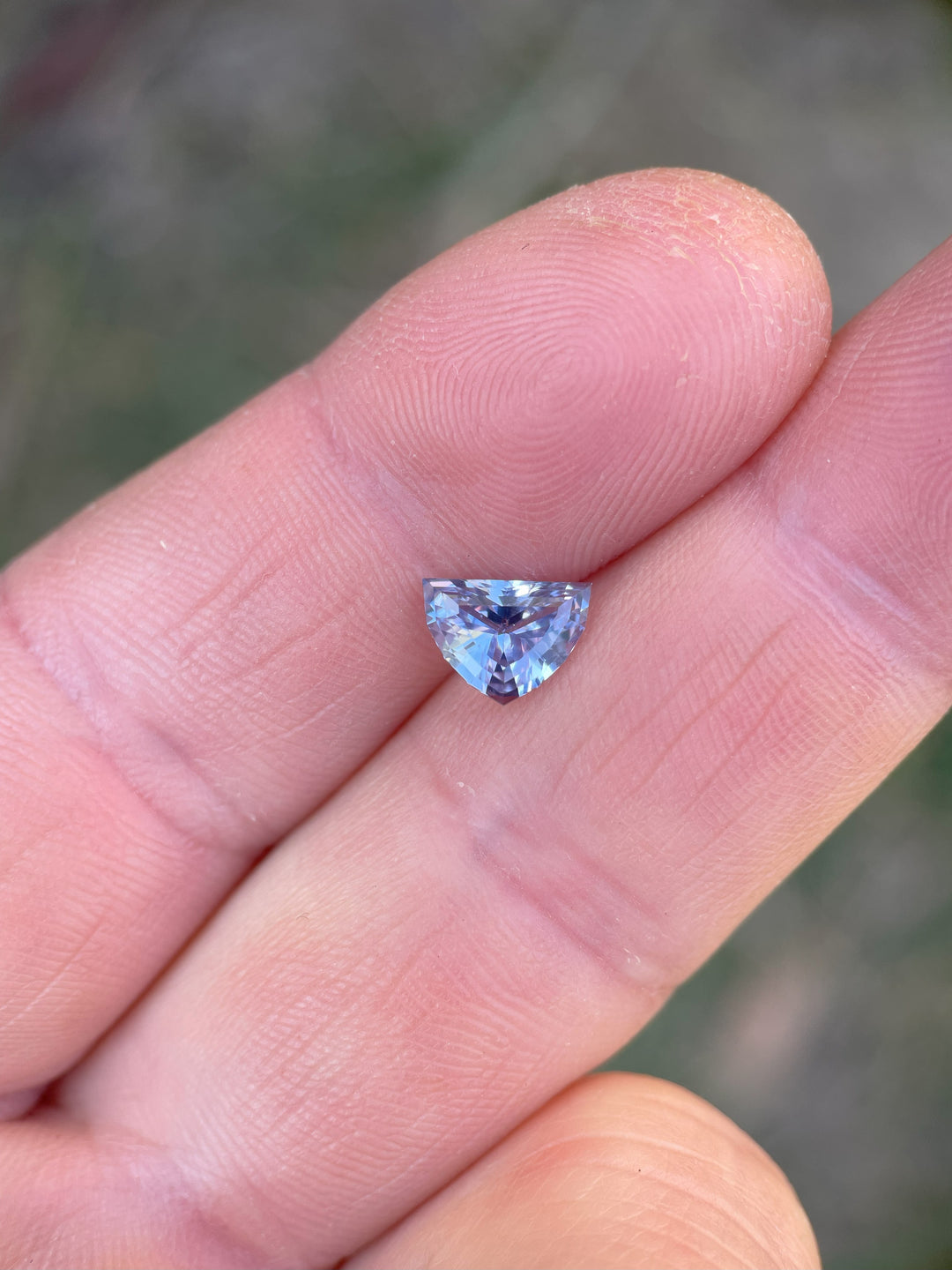 1.66-carat periwinkle sapphire held between fingers, showcasing its unique antique-style arrow cut and brilliant sparkle.