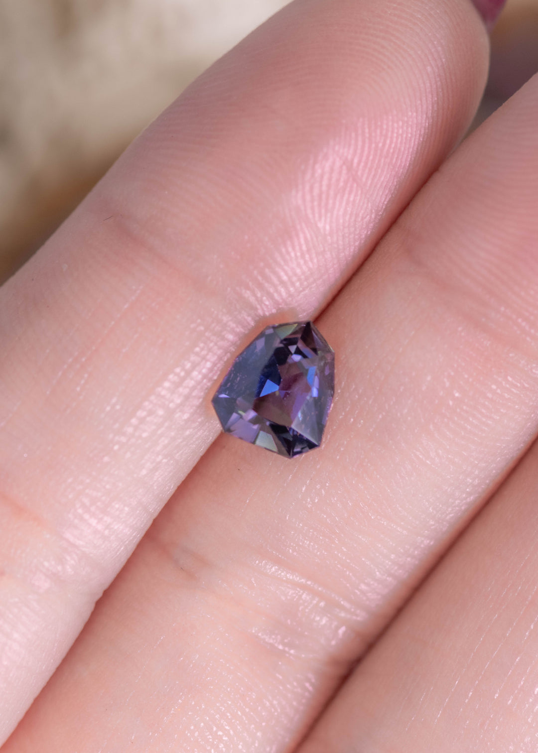 1.66 carat teal green blue purple Tanzanite custom shield modified brilliant resting on finger, precision faceted gemstone from Merelani Hills Tanzania showing sharp geometric facets, color shift and sparkle for custom jewelry