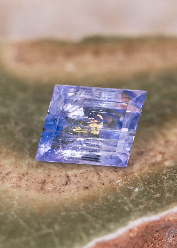 Natural 1.67 carat emerald cut Tanzanite gemstone on stone surface showing purple blue green mermaid color and eye clean clarity