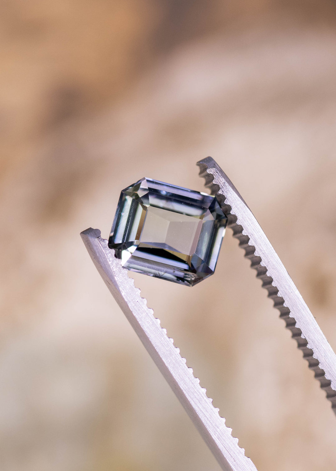 1.67 carat teal blue green purple Tanzanite modified emerald cut held in tweezers, precision faceted gemstone from Merelani Hills Arusha Tanzania displaying crisp geometric symmetry, tablet depth profile and strong step facet reflections