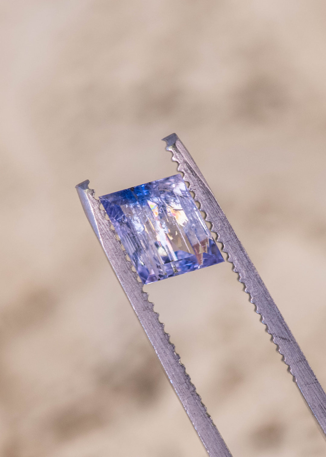 1.67 carat emerald cut Tanzanite gemstone in mermaid purple blue green color held in gem tweezers showing natural brilliance and step cut facets