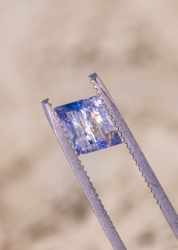 1.67 carat emerald cut Tanzanite gemstone in mermaid purple blue green color held in gem tweezers showing natural brilliance and step cut facets