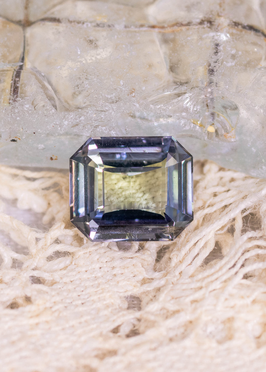 1.67 carat teal blue green purple Tanzanite custom modified emerald cut displayed on natural stone surface, Merelani Hills Tanzania gemstone showing clean step facets, beveled corners and vivid color shift for custom jewelry design
