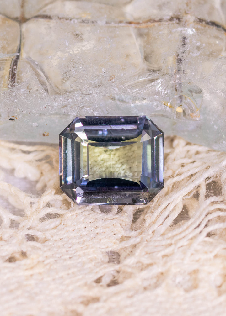 1.67 carat teal blue green purple Tanzanite custom modified emerald cut displayed on natural stone surface, Merelani Hills Tanzania gemstone showing clean step facets, beveled corners and vivid color shift for custom jewelry design