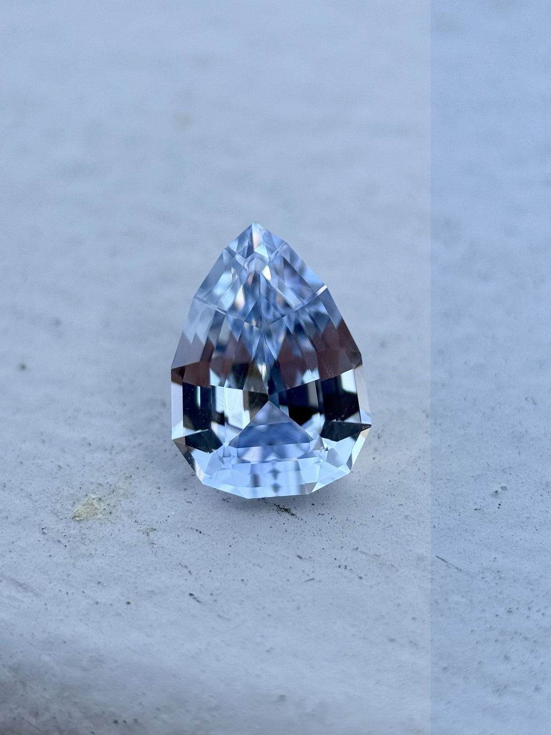 Close-up of a 1.67-carat unheated cornflower and powder blue sapphire in geometric pear brilliant cut from Sri Lanka, sitting on a stone surface