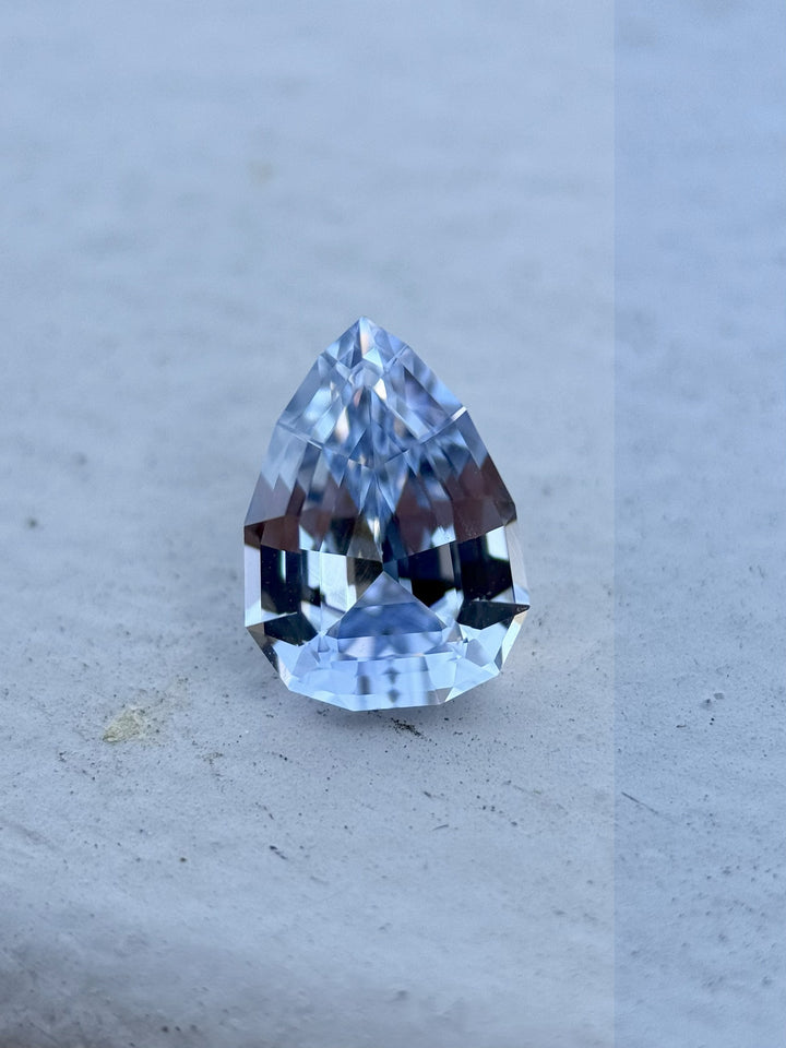 Close-up of a 1.67-carat unheated cornflower and powder blue sapphire in geometric pear brilliant cut from Sri Lanka, sitting on a stone surface
