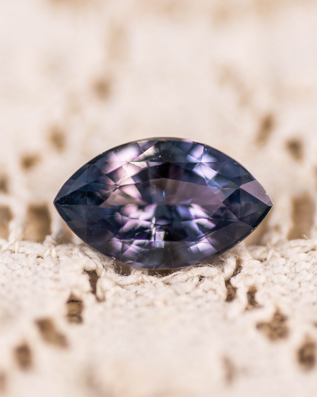 1.68 carat pinkish gray violet sapphire resting on textured lace, showcasing subtle color shift and internal brilliance of the precision marquise mixed cut, untreated gemstone from Sakaraha, Madagascar.