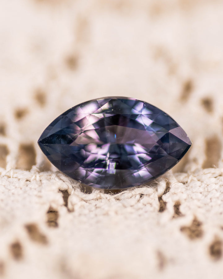 1.68 carat pinkish gray violet sapphire resting on textured lace, showcasing subtle color shift and internal brilliance of the precision marquise mixed cut, untreated gemstone from Sakaraha, Madagascar.