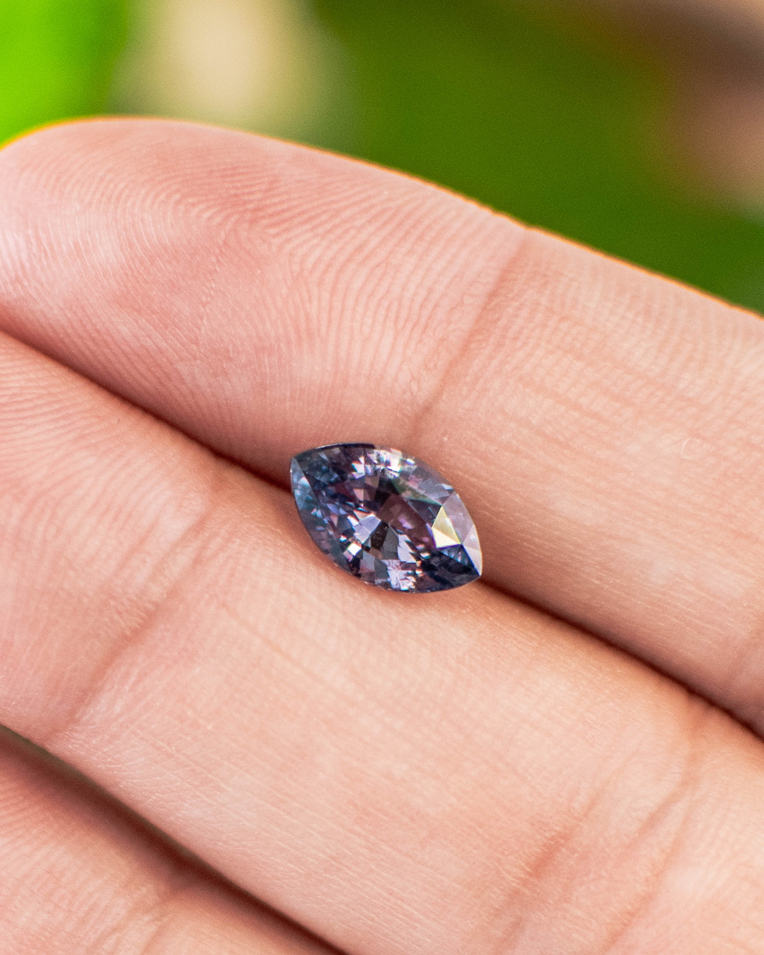 1.68 carat violet-gray sapphire displayed on fingertips, showing its delicate color shift and luster of the precision marquise mixed cut, untreated gemstone from Sakaraha, Madagascar.