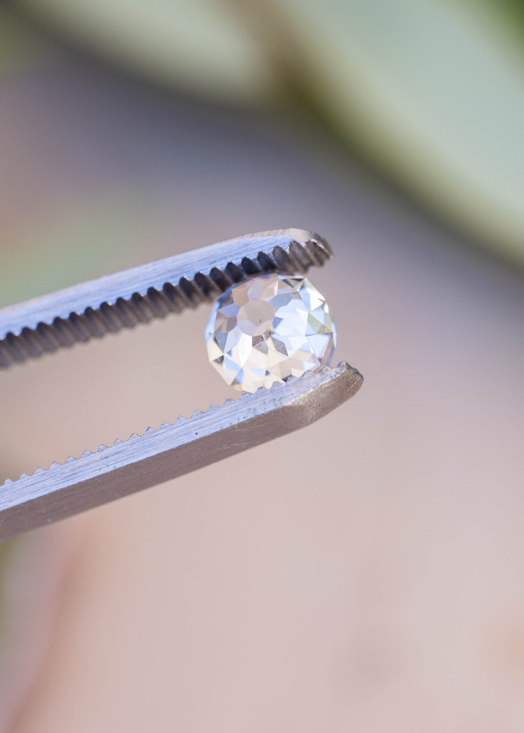 Angled view of the 1.68 carat diamond in tweezers, highlighting its softly rounded outline, deep profile and hand-worked appearance.