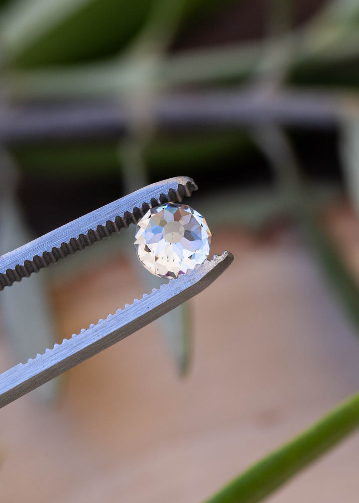 Mughal cut diamond held outdoors in tweezers, reflecting soft silver, champagne and cool blue tones in natural light.