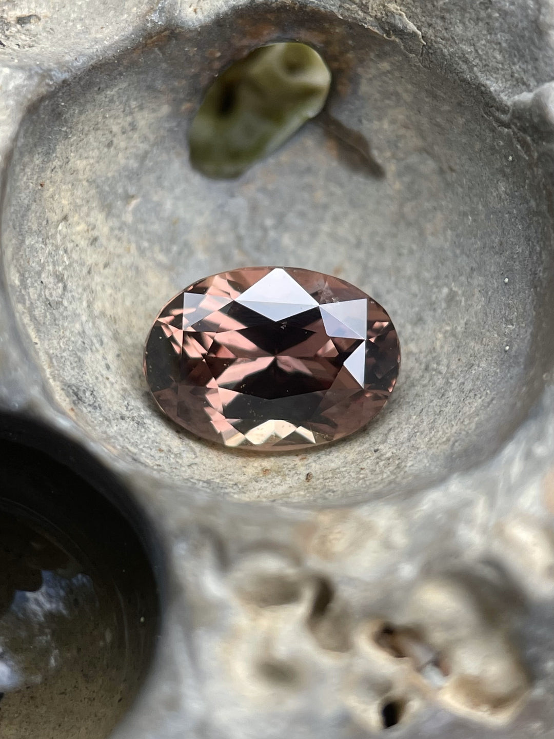 A 1.68-carat color-change sapphire with hues of purplish pink and brownish pink, placed in a textured carved stone setting to highlight its warm tone and brilliance.
