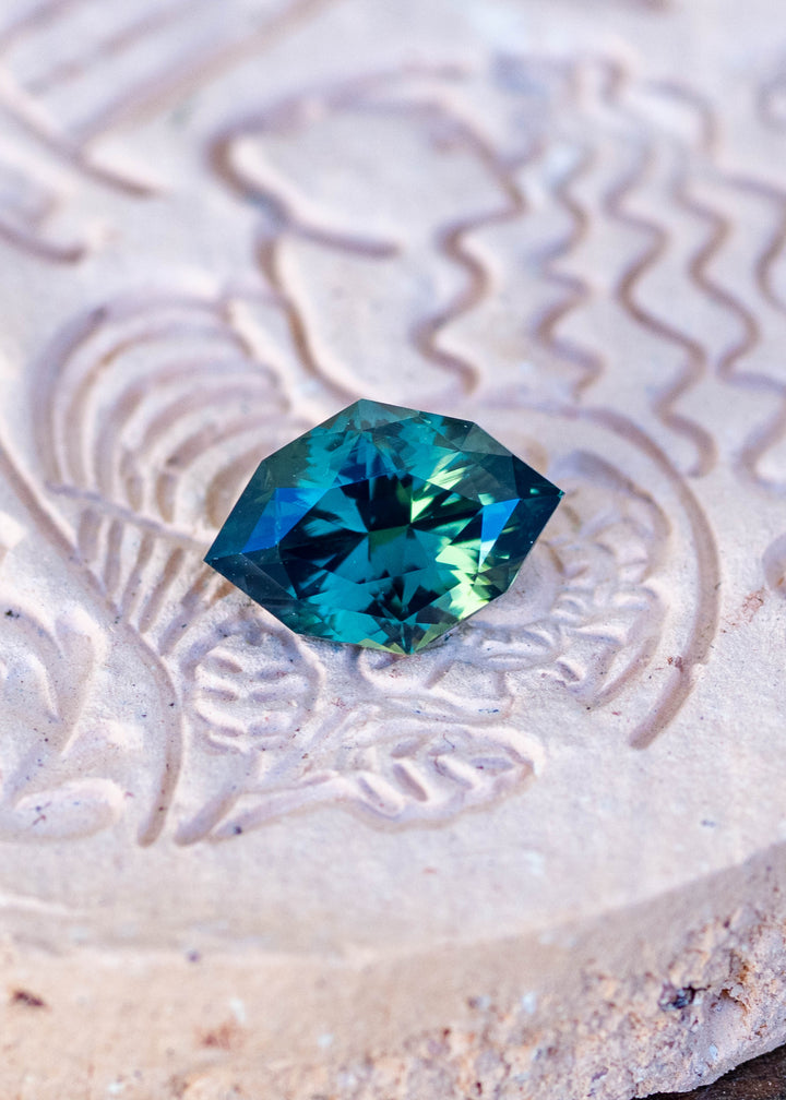 1.68ct green teal geometric marquise sapphire from Diego, Madagascar resting on a carved stone.