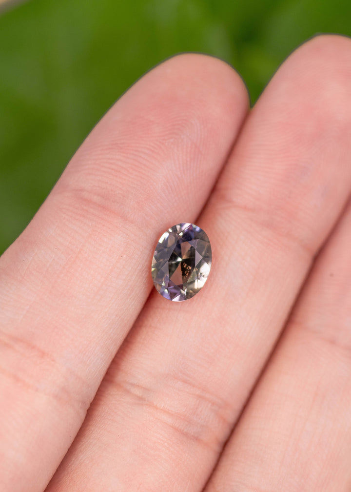 1.69 carat blue purple yellow Tanzanite mix modified brilliant oval resting on finger, precision faceted gemstone from Merelani Hills Tanzania showing trichroic color shift, brilliance and clarity for custom jewelry