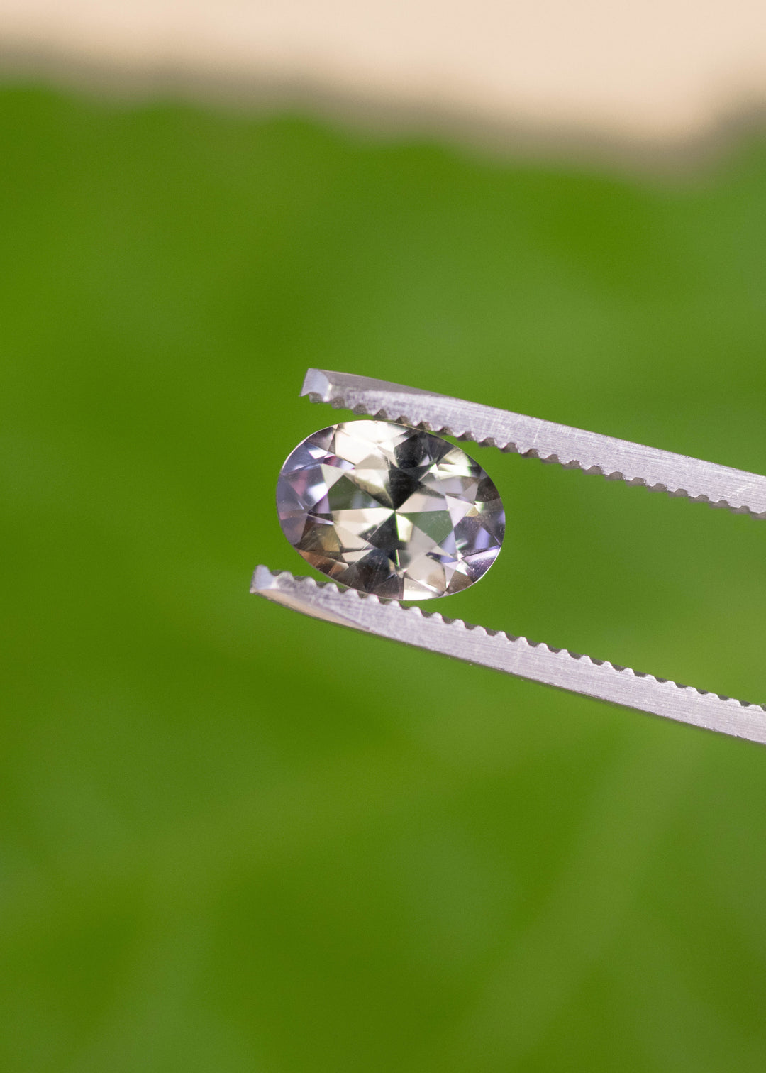 1.69 carat blue purple yellow Tanzanite oval held in tweezers, mix modified brilliant cut gemstone from Merelani Hills Arusha Tanzania displaying sparkle, sharp facet reflections and natural color variation for fine jewelry design