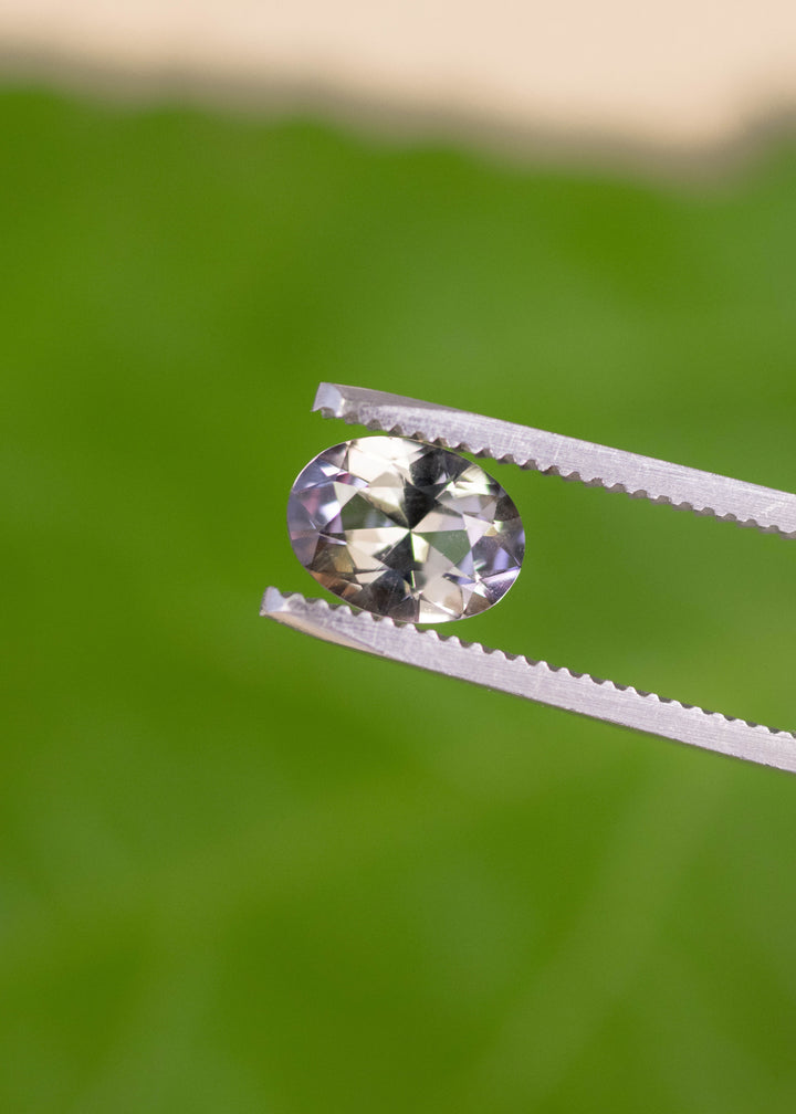 1.69 carat blue purple yellow Tanzanite oval held in tweezers, mix modified brilliant cut gemstone from Merelani Hills Arusha Tanzania displaying sparkle, sharp facet reflections and natural color variation for fine jewelry design