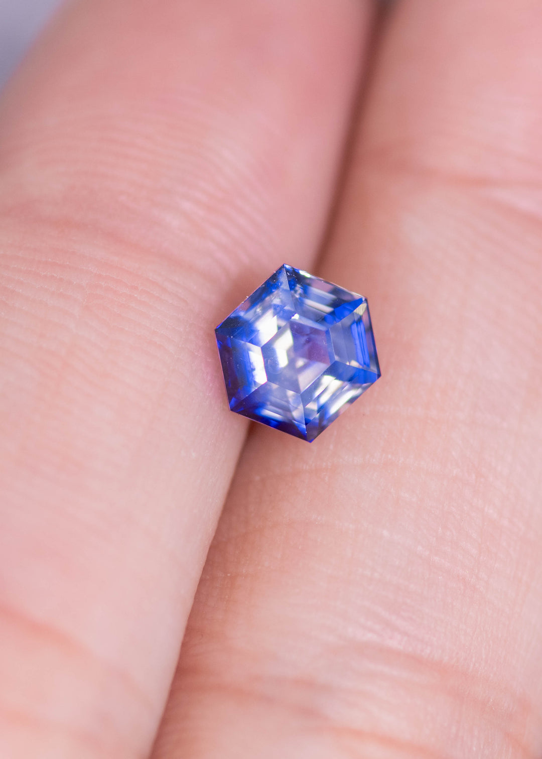 Loose bi‑color blue and colorless sapphire resting on a fingertip for scale, showing the custom geometric hexagon step cut and natural untreated color from Sri Lanka.