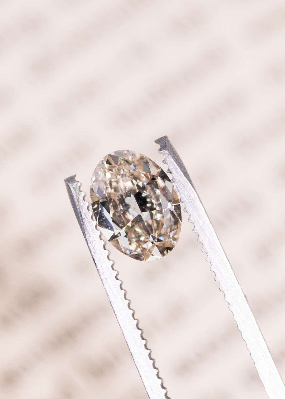 Loose oval diamond with light rosy brown color held in tweezers showing brilliance and facet pattern, Canadian diamond gemstone.