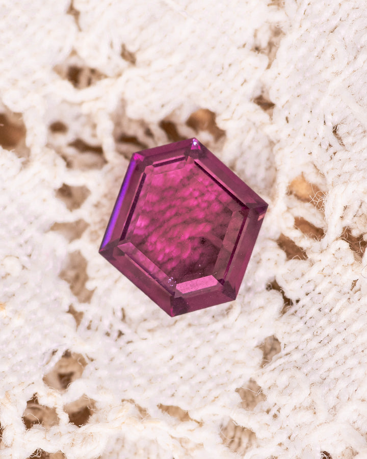 1.71 carat pink and purple garnet resting on soft white fabric, displaying striking clarity and faceting detail of the custom geometric step cut tablet, untreated garnet from Kenya.