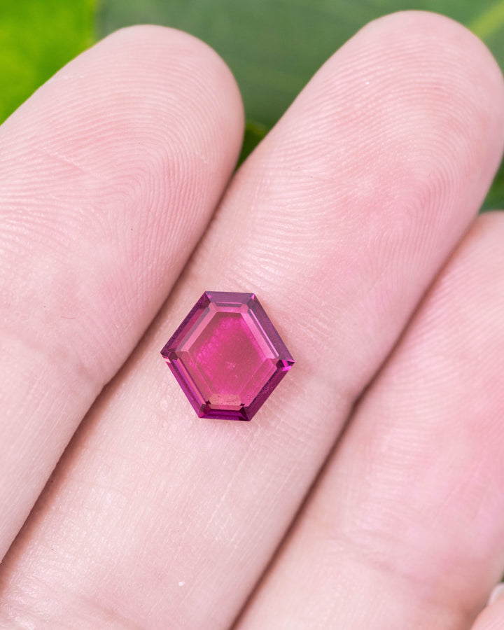 1.71 carat pink and purple garnet displayed on fingertips, capturing light reflections, brilliance, and fine craftsmanship of the custom geometric step cut tablet, untreated garnet from Kenya