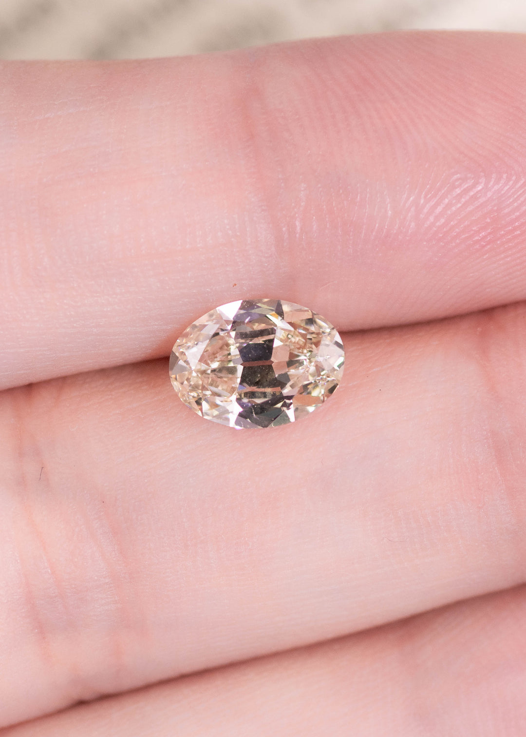 1.71 carat oval diamond resting on finger showing size and soft rosy brown tone, loose diamond for engagement ring or jewelry.