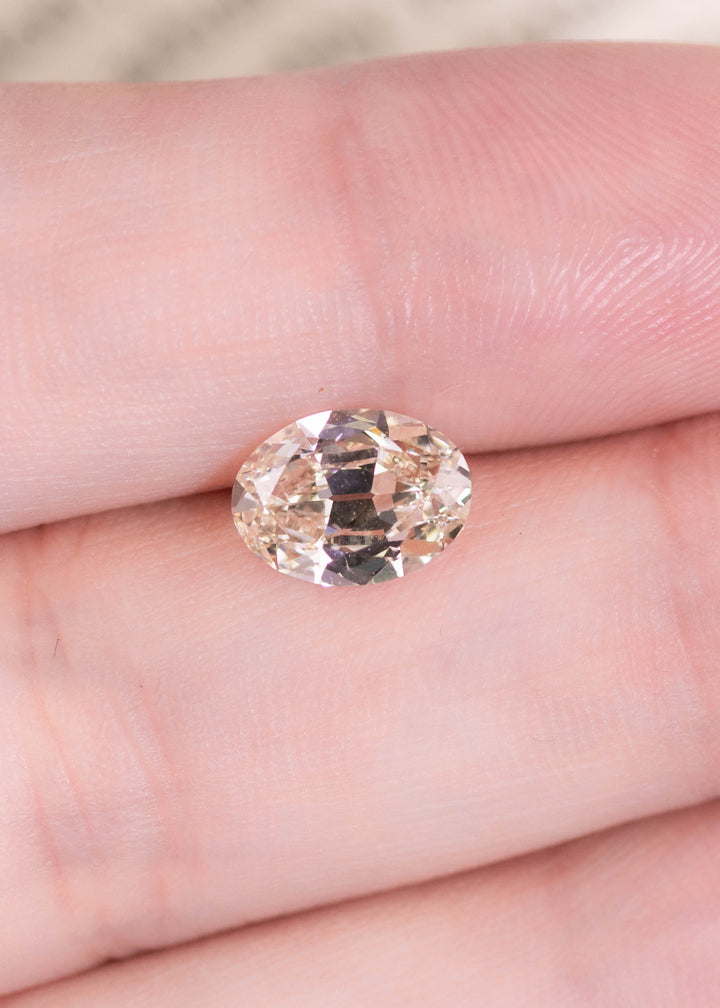 1.71 carat oval diamond resting on finger showing size and soft rosy brown tone, loose diamond for engagement ring or jewelry.