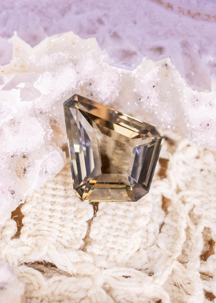 Natural 1.72 carat Tanzanite custom kite step cut on fabric and druzy crystal surface showing golden yellow hues and precision faceting