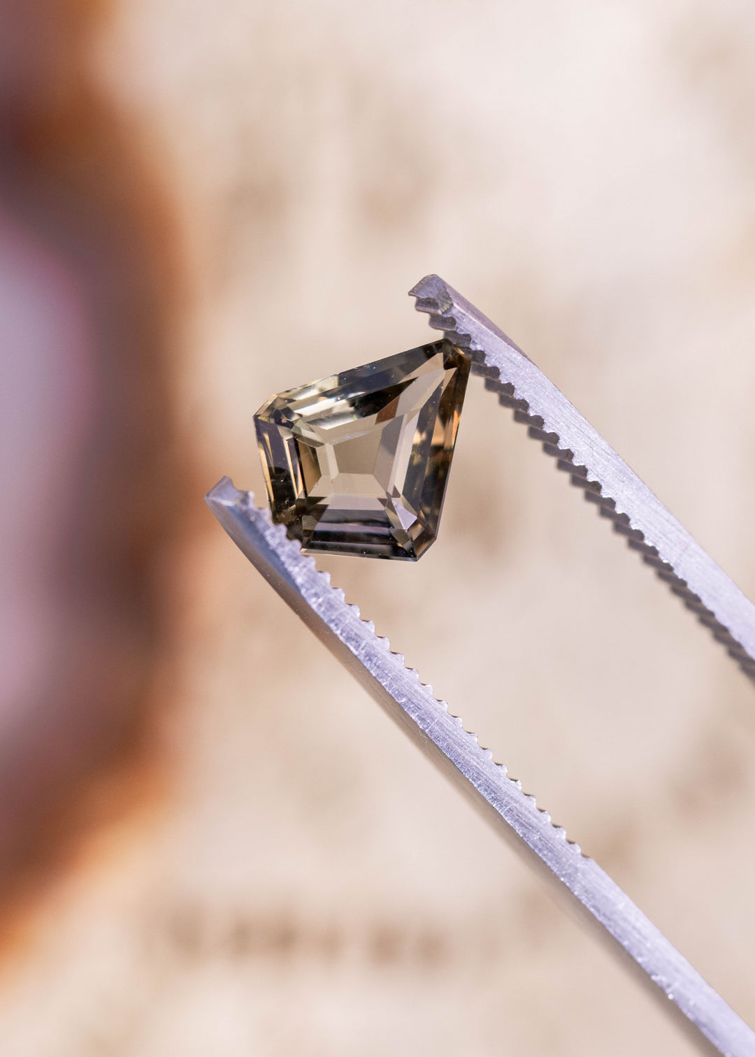 1.72 carat custom kite step cut Tanzanite in golden teal yellow colors held in gem tweezers showing geometric facets and brilliance