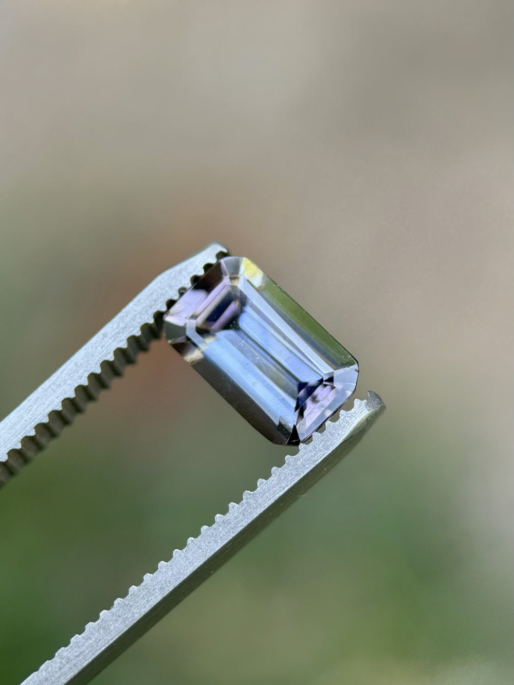 Emerald cut Tanzanite gemstone displaying mermaid tones of blue, teal, yellow, and pink in natural light