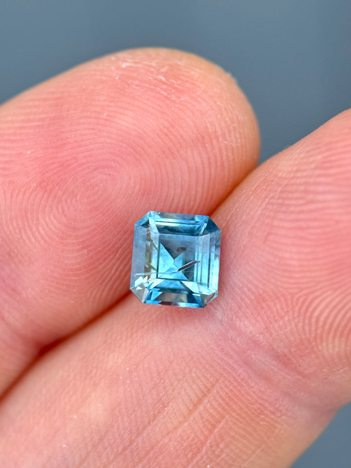 Close-up of heated El Dorado Bar sapphire resting on finger tips displaying hall-of-mirrors effect and cool sky-blue tones.