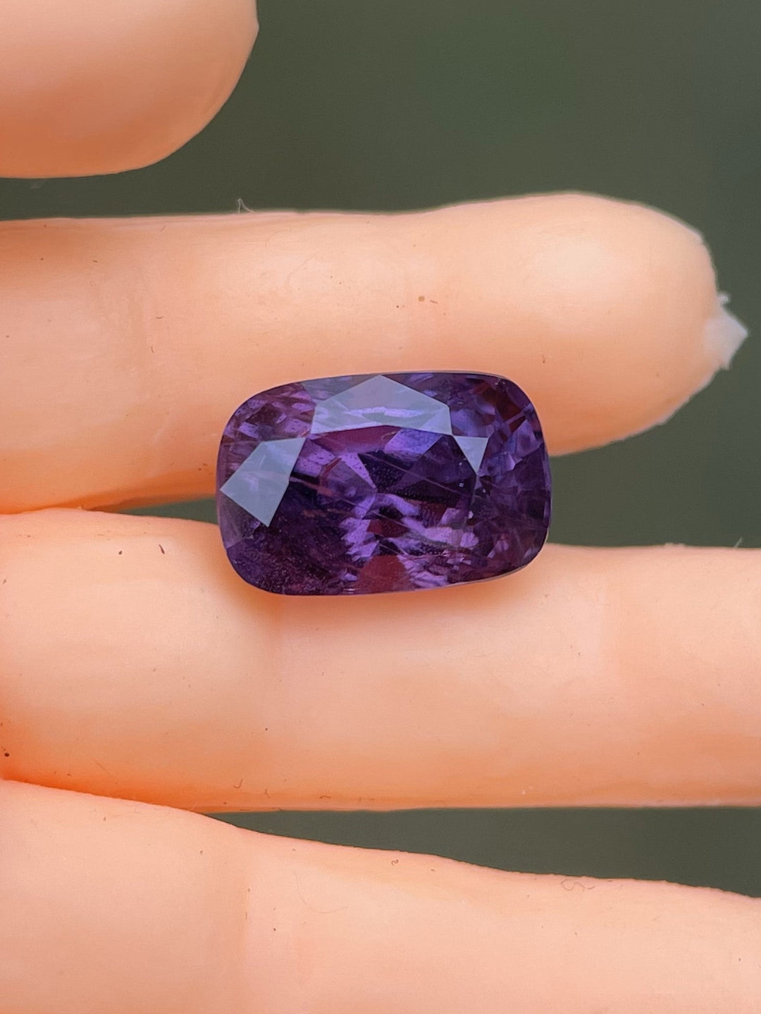 A 1.75-carat mix cushion cut sapphire in shades of pink and mulberry, resting on a mannequin hand. The gemstone displays deep, rich hues and high clarity, highlighting the natural brilliance of the sapphire from Luc Yen, Vietnam, untreated and ready for fine jewelry settings.