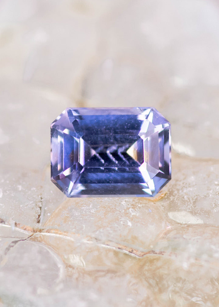 Natural 1.76 carat Tanzanite gemstone on sea glass showing blue purple hues clarity and precision modified emerald cut faceting