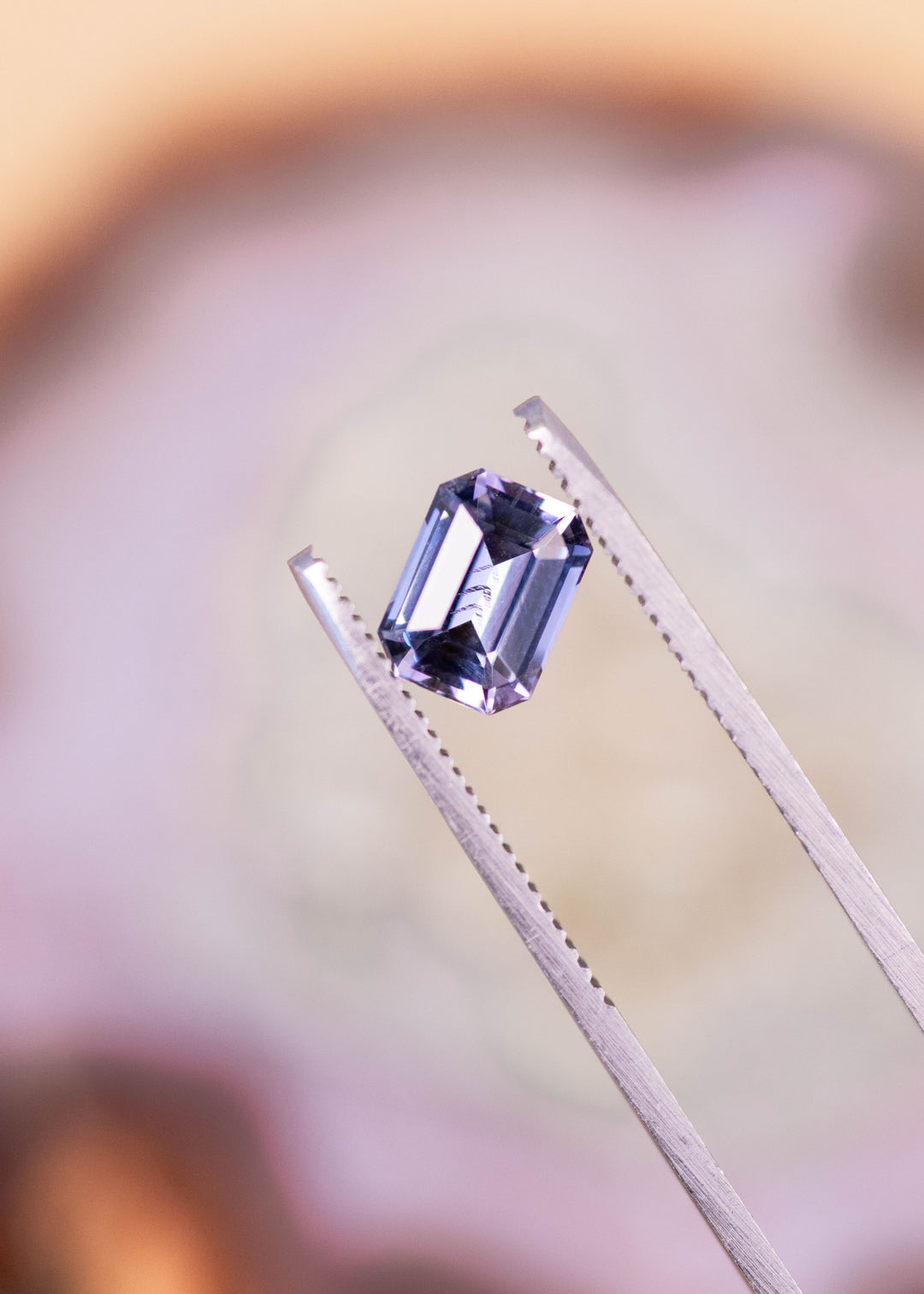 1.76 carat blue purple Tanzanite modified emerald cut held in gem tweezers showing step cut facets and natural unheated brilliance from Tanzania