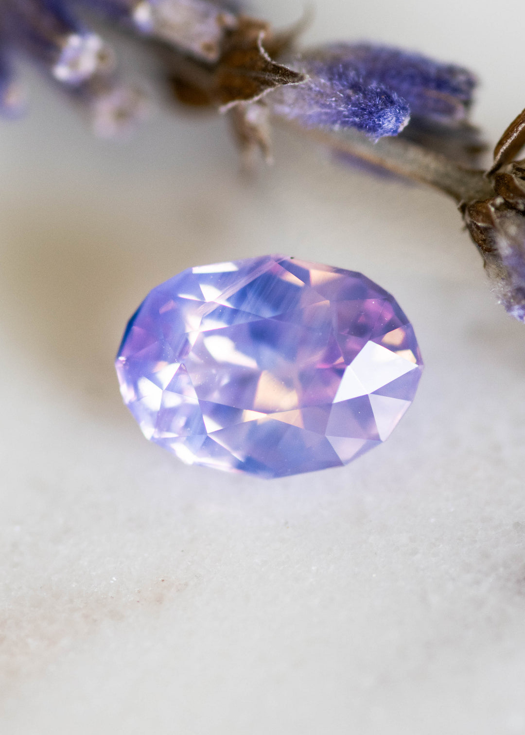 Loose 1.78 carat opalescent purplish pink sapphire from Ratnapura shown face-up on a white surface, displaying the precision oval mix cut and soft lavender-pink glow.