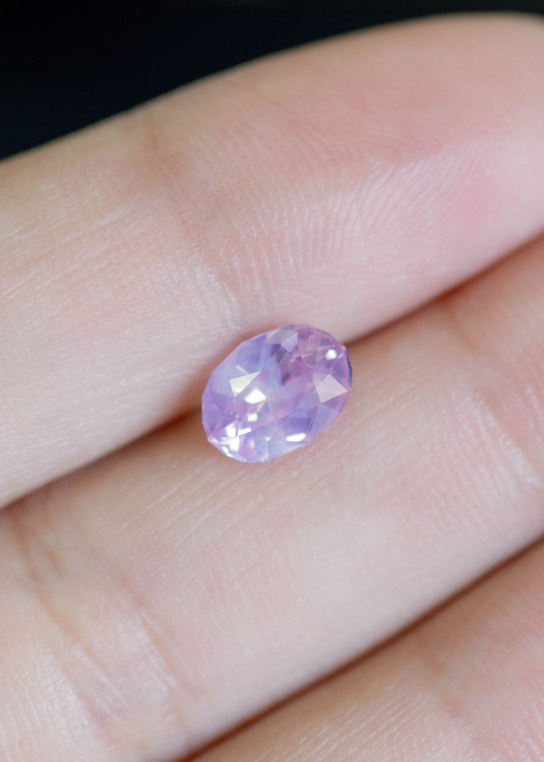Loose 1.78 carat purplish pink oval sapphire resting on fingertips, revealing its opalescent body color and reflective mix-cut faceting.