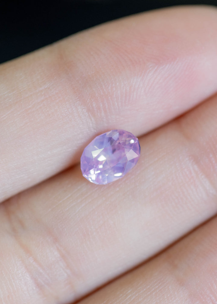 Loose 1.78 carat purplish pink oval sapphire resting on fingertips, revealing its opalescent body color and reflective mix-cut faceting.