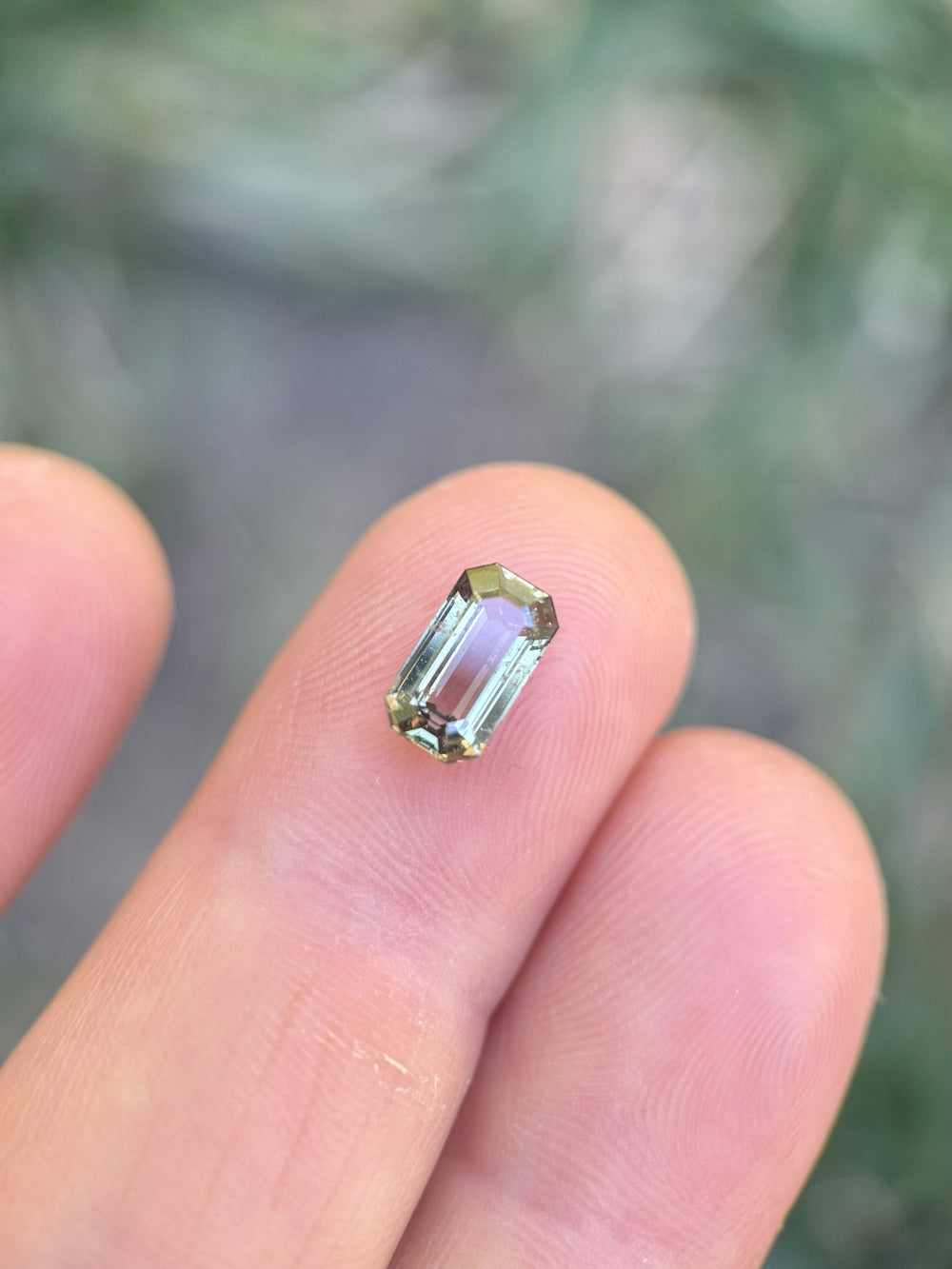 1.80ct earthy teal green sapphire in antique emerald cut displayed on fingertips, showing natural clarity and luster
