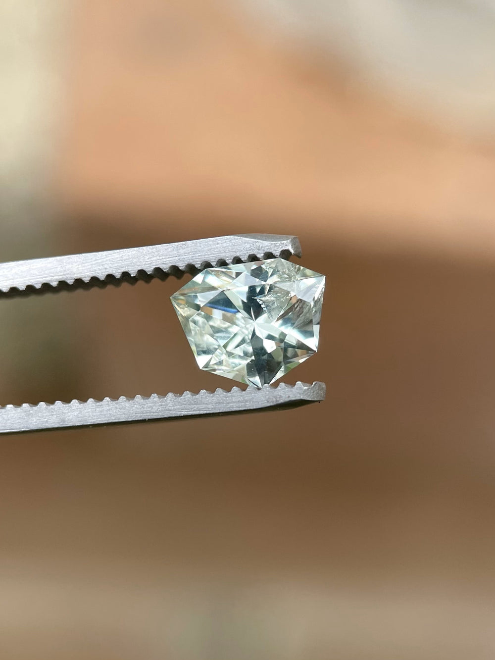 1.80 carat trillion cut sapphire in yellow, green, and blue hues held in tweezers, unheated and sourced from Chimwadzulu Hill, Malawi.
