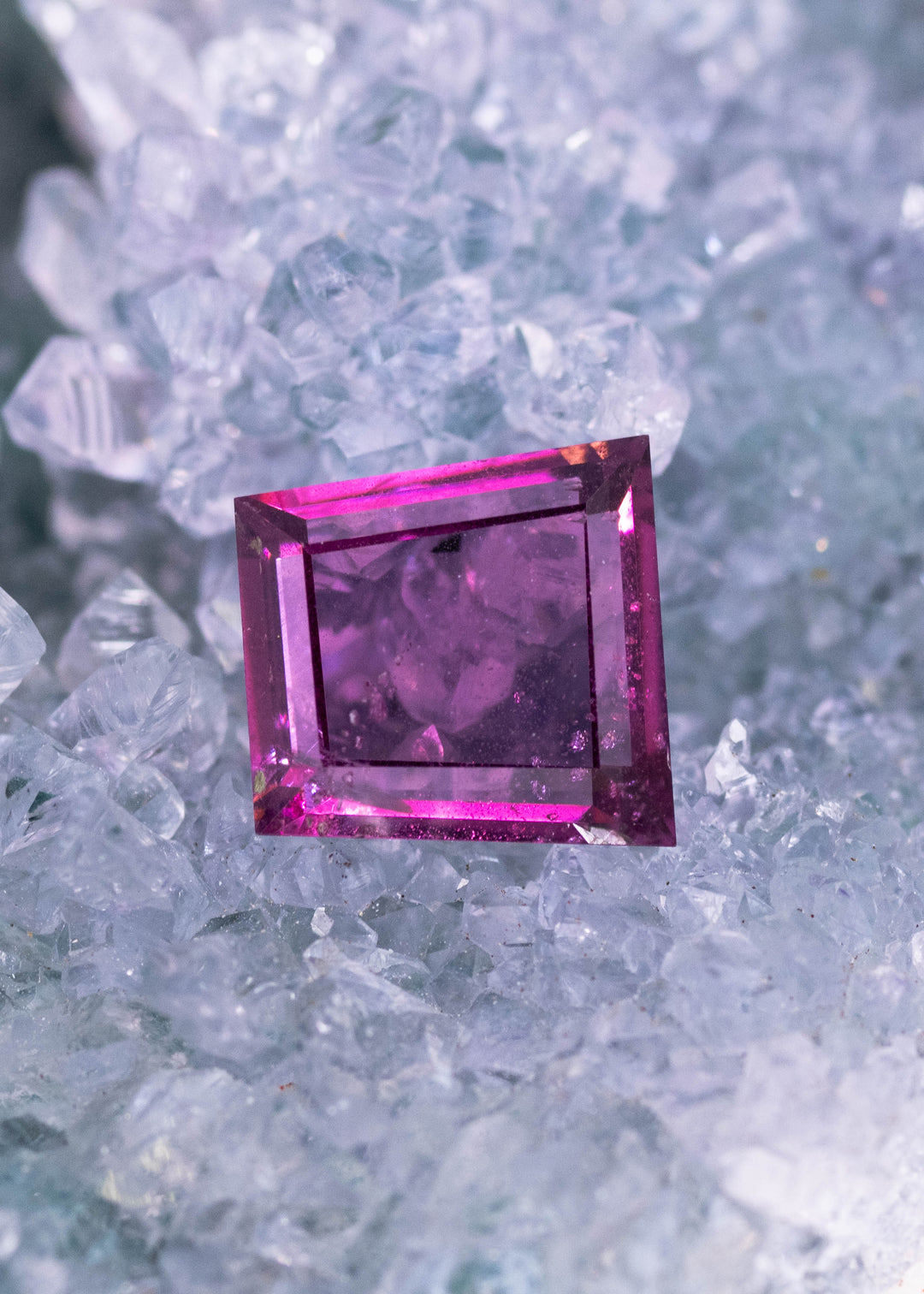 1.83ct pink and purple natural portrait  cut garnet gemstone from Kenya displayed face up on a natural blue crystal surface.