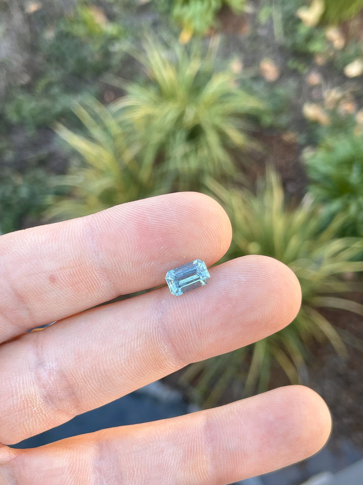 A 1.84-carat seafoam blue emerald-cut aquamarine gemstone resting on a fingertip, showcasing its clean cut and sparkling color.