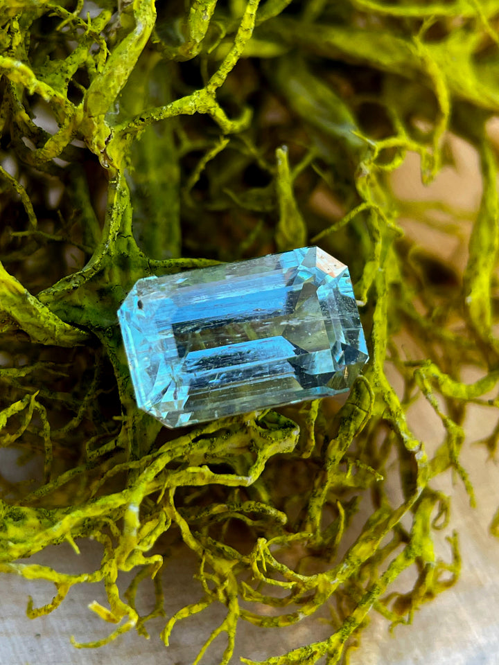 Close-up of a 1.84-carat emerald-cut aquamarine gemstone nestled in vibrant green moss, highlighting its seafoam blue hue and natural beauty.