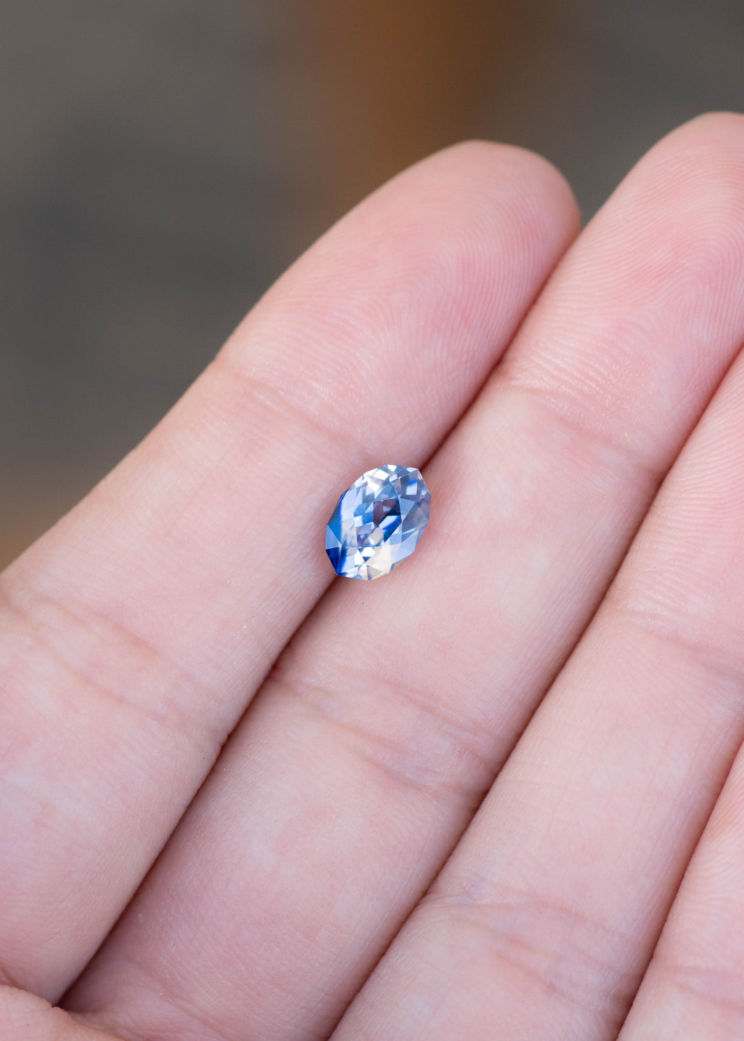 1.85ct blue and white parti sapphire in a custom moval brilliant cut from Sri Lanka held on finger tips to show color and scale.