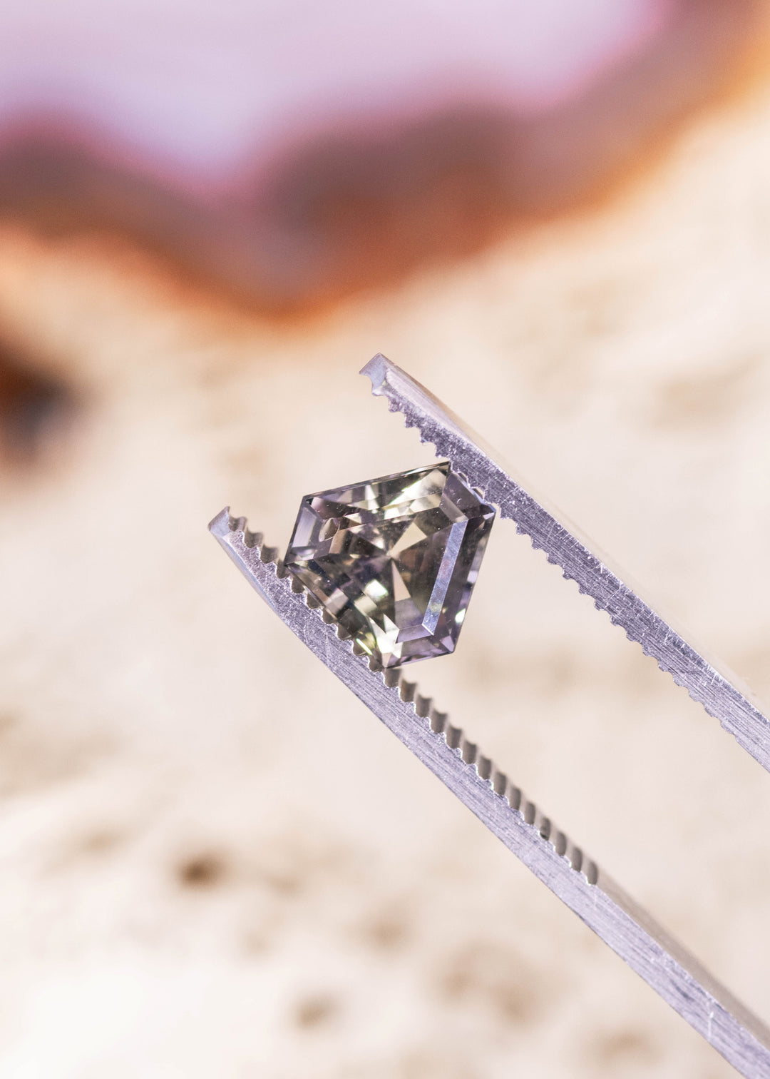 1.87 carat fancy peach lavender Tanzanite custom calf head step cut held in gem tweezers showing unique faceting and color shift from Tanzania