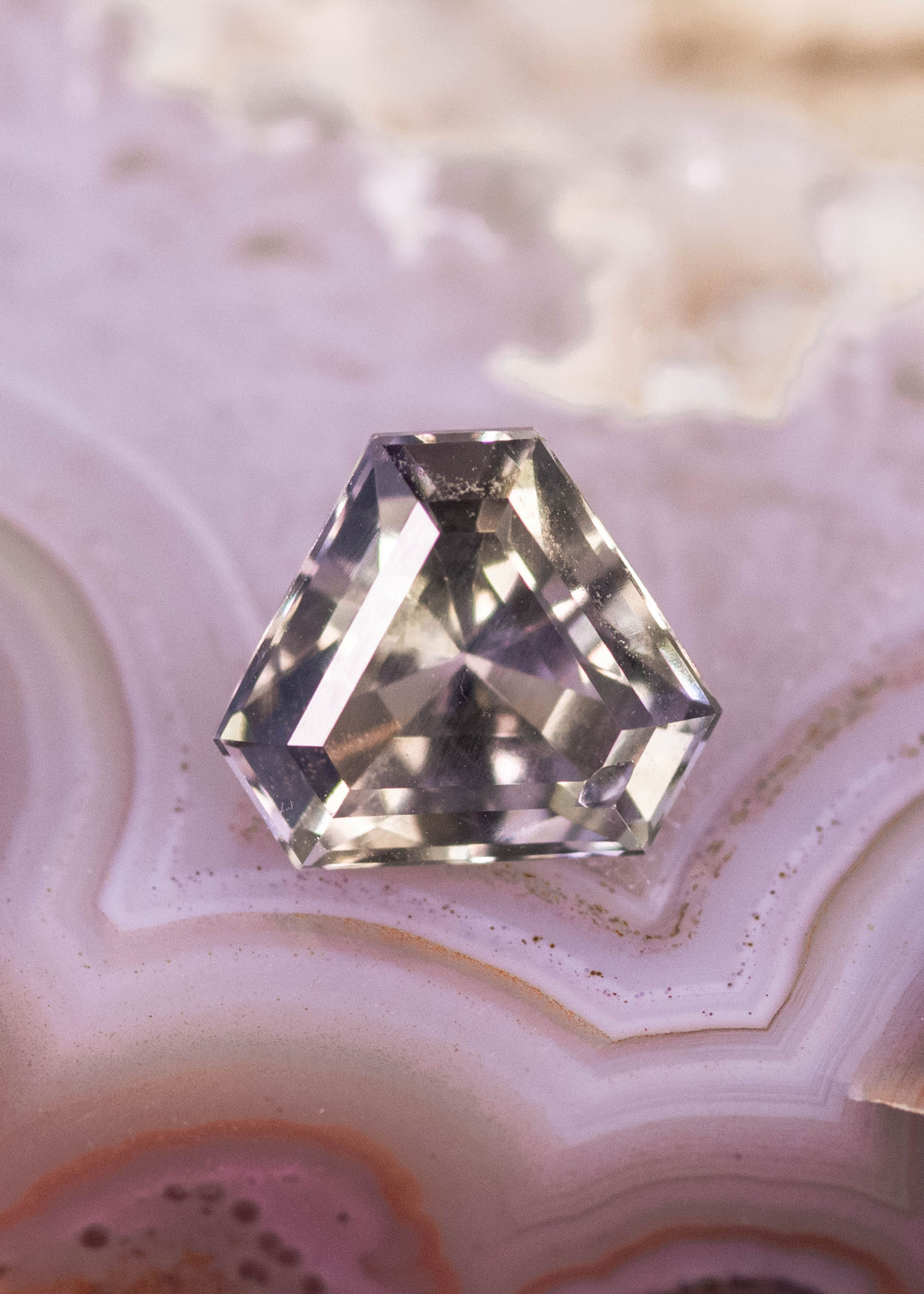 Natural 1.87 carat Tanzanite gemstone on agate surface showing fancy peach and lavender hues with precision custom step cut faceting