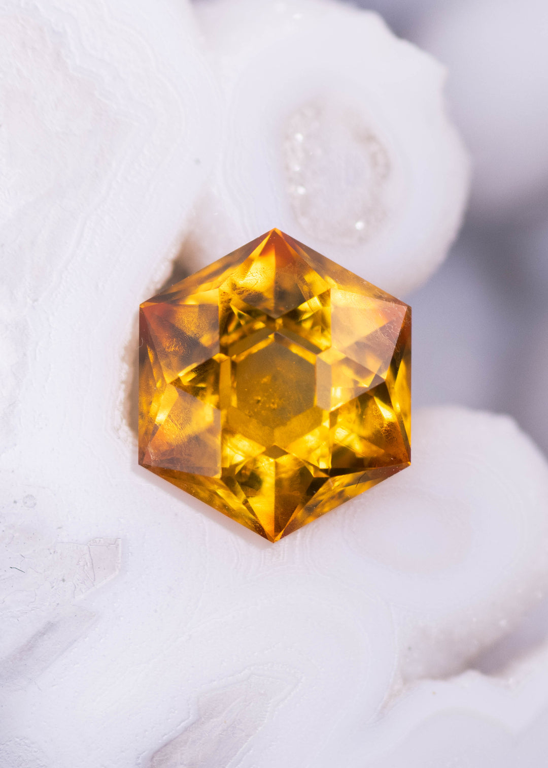 1.88 carat orange yellow Montana sapphire hexagonal modified brilliant cut resting on white crystal background showing fiery golden brilliance from El Dorado Bar Deposit, heated