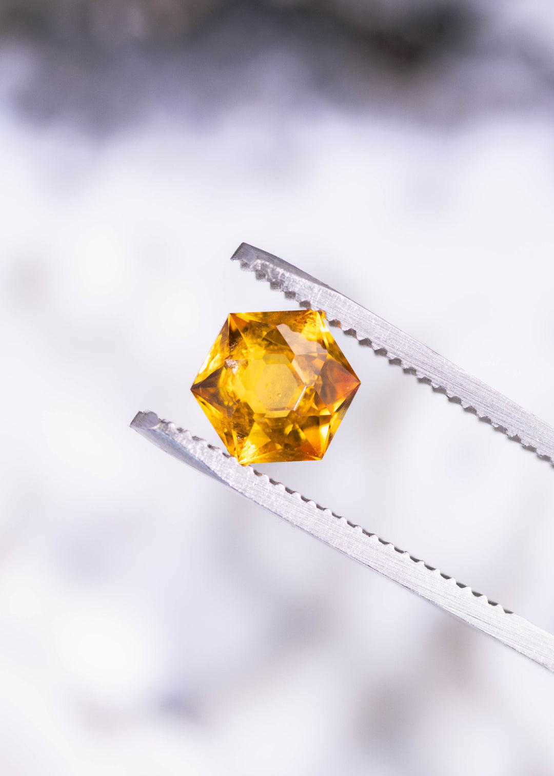 1.88ct orange Montana sapphire hexagonal brilliant cut held in tweezers displaying bright yellow flashes and geometric facet pattern from El Dorado Bar, heated