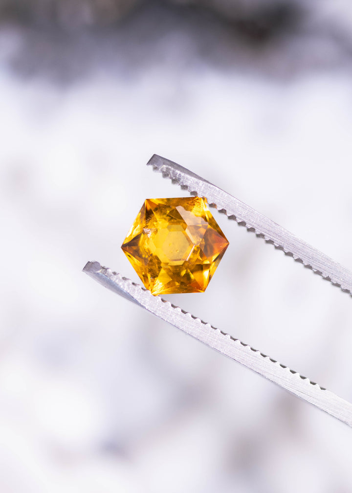 1.88ct orange Montana sapphire hexagonal brilliant cut held in tweezers displaying bright yellow flashes and geometric facet pattern from El Dorado Bar, heated